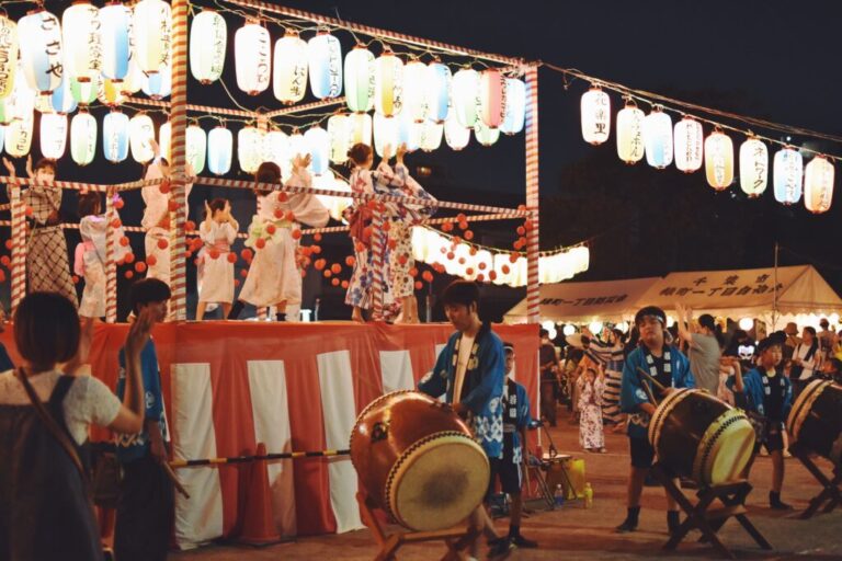 提灯が灯る櫓の上で踊る浴衣姿の参加者と太鼓演奏