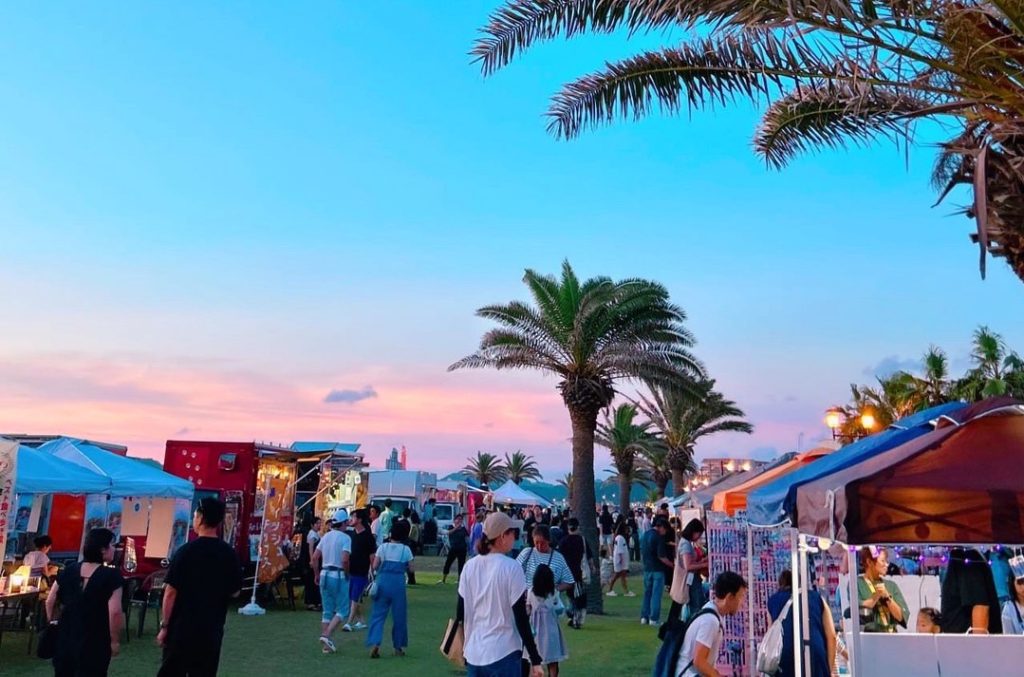 夕暮れ空とヤシの木に囲まれたHOJO BEACH MARKETの会場。キッチンカーや雑貨ブースが並び来場者で賑わう
