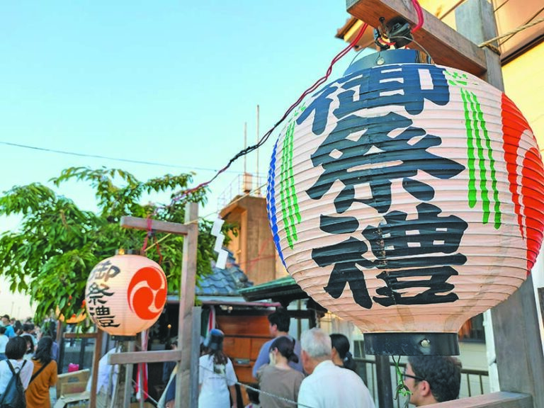 夕暮れ時の湊水神宮境内に掲げられた御祭禮の提灯と参拝客の様子