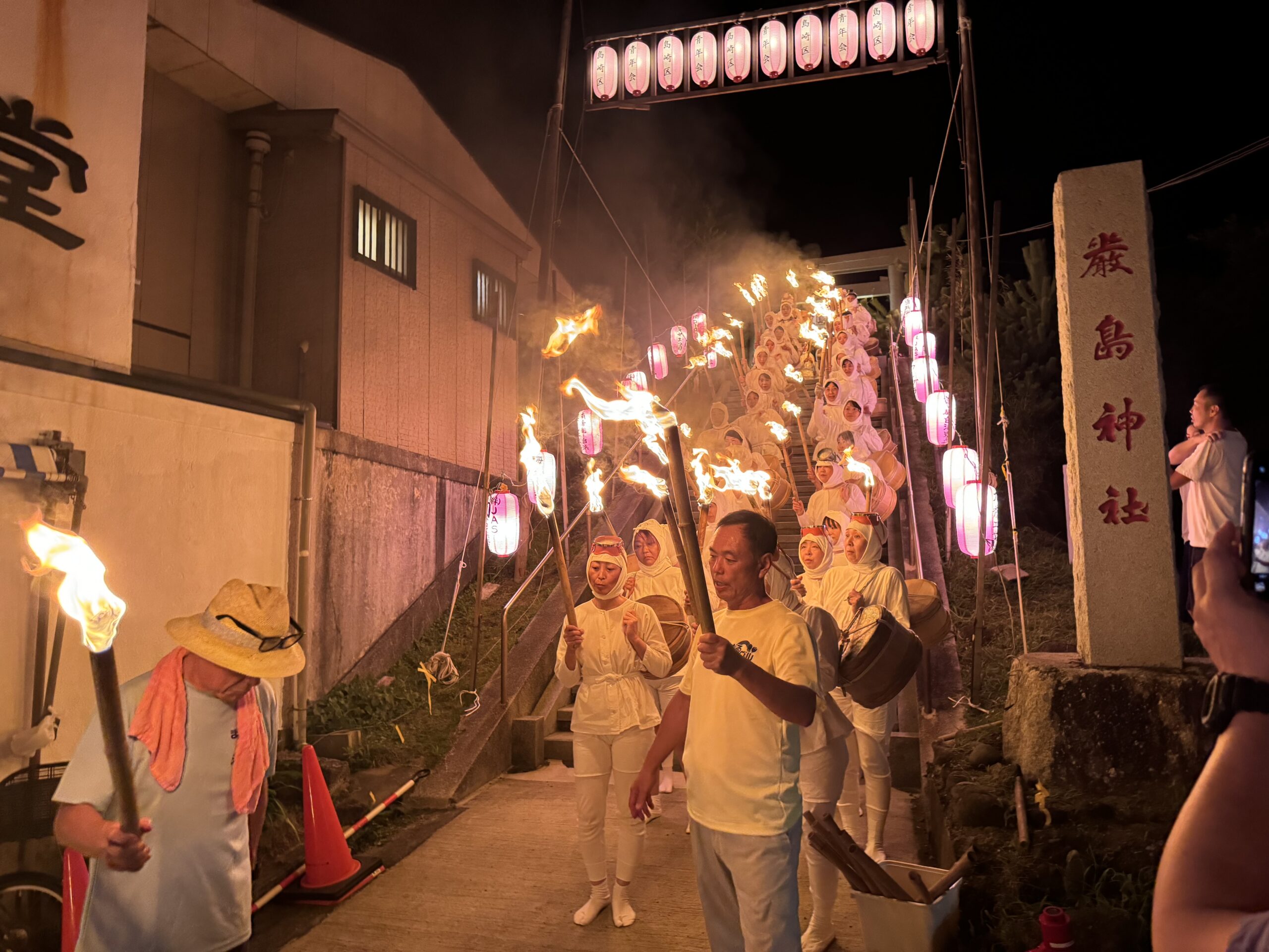 厳島神社の石段を松明と桶を持って下りてくる白装束の海女たちの行列