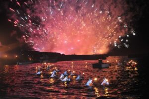 野島埼沖の夜空に上がる花火と、海面で松明の灯をともして泳ぐ海女たちの大夜泳