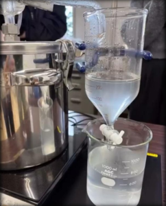 IHコンロに載ったステンレス製の蒸留釜から配管が伸び、分液ロートを通って1000mlのガラスビーカーに透明な液体が落ちている
