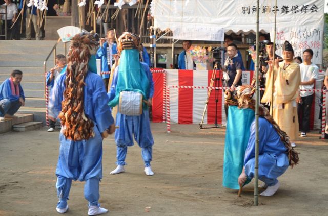 別所地蔵寺の境内で舞う獅子3匹。石段と紅白幕、笛師や僧侶、見物客が写る