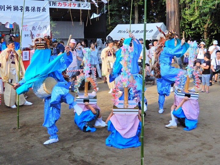 青竹を立てた花場で舞う別所の獅子舞と花笠持ちの小学生