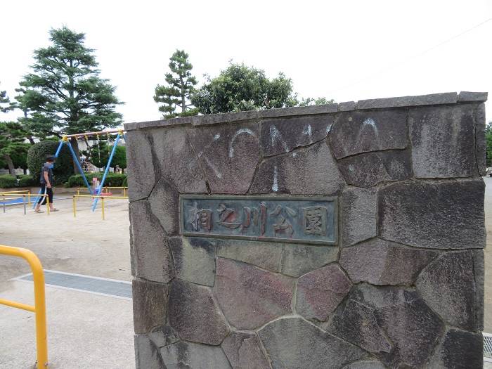 「相之川公園」と刻まれた石の銘板が入った公園入口の門柱。奥にブランコ