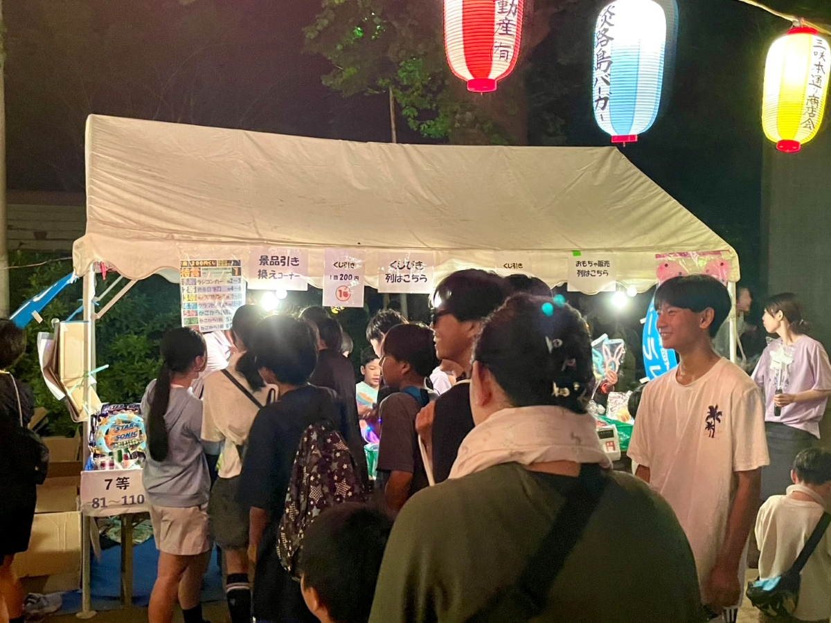 盆踊り会場のくじびきコーナーに親子連れが列を作る夜の様子
