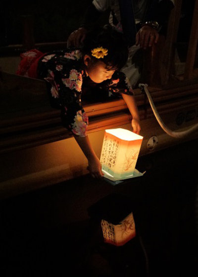 浴衣姿の女の子が、願い事を書いた白い灯ろうを小野川の水面にそっと流す様子