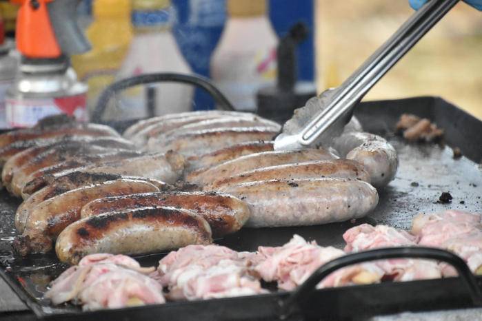 大きな鉄板の上で焼き色のついたソーセージが並び、トングで返されている。手前には生の豚肉が置かれている