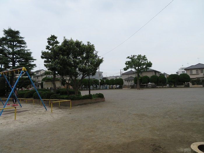 相之川公園の広場。ブランコと刈り込まれた樹木、奥に住宅街が広がる