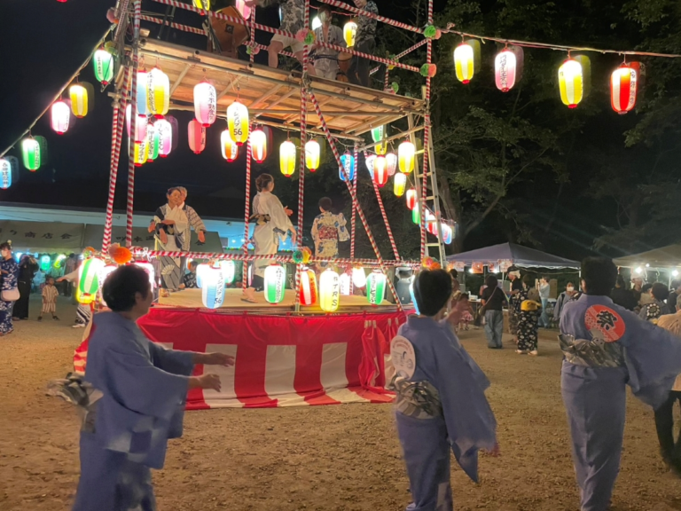 三咲稲荷神社の紅白幕を巻いた櫓を囲み、青い浴衣の踊り手が輪になって踊る盆踊り