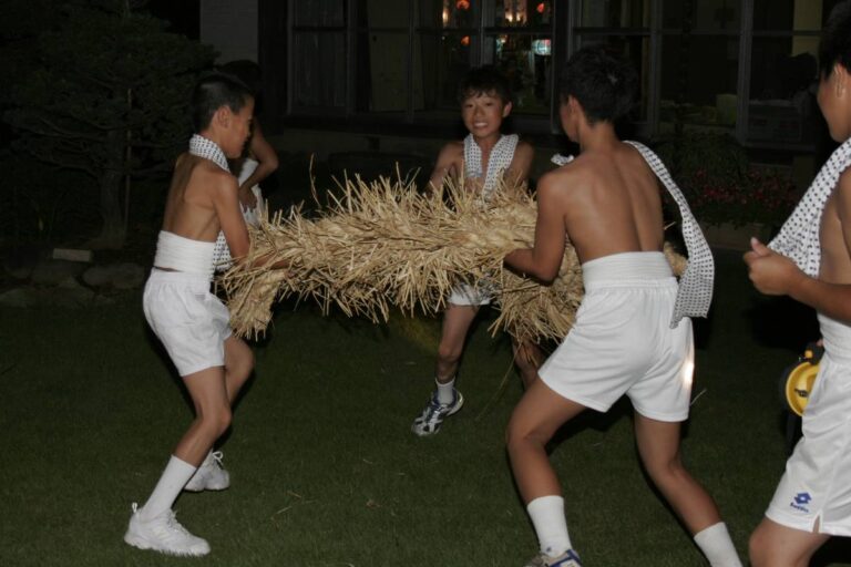 夜、豆絞りの手ぬぐいを肩にかけ白い短パン姿の少年たちが、藁を束ねて編んだ太い綱を数人がかりで抱え、芝生の上を進んでいる。背後は明かりの灯った建物のガラス窓