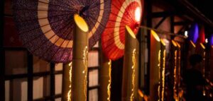 竹筒に入った灯りと、紫・赤の和傘が並ぶ、佐原の夜の町並み。竹には光の粒が連なる