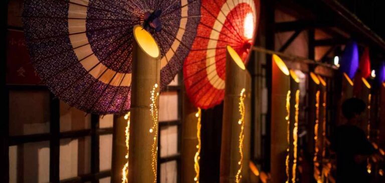 竹筒に入った灯りと、紫・赤の和傘が並ぶ、佐原の夜の町並み。竹には光の粒が連なる