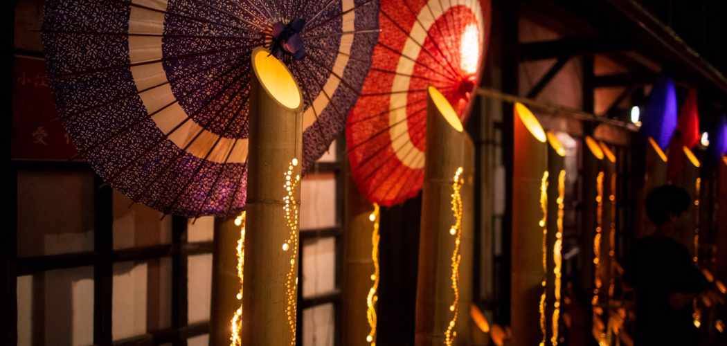 竹筒に入った灯りと、紫・赤の和傘が並ぶ、佐原の夜の町並み。竹には光の粒が連なる