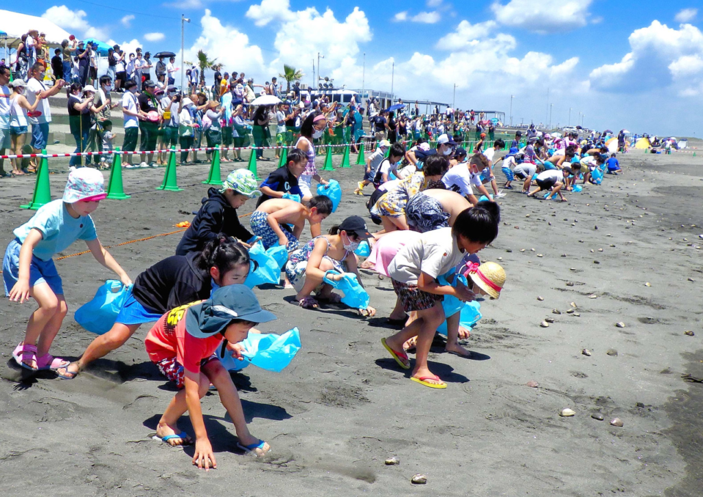 一宮海水浴場の砂浜で、青い袋を持った大勢の子どもたちが一斉にはまぐりを拾う南九十九里はまぐり祭りの様子