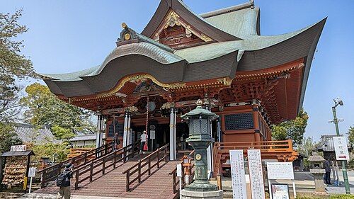 朱塗りの柱と緑青色の屋根をもつ布施弁天の本堂を、石段の下から斜め正面に見上げた様子