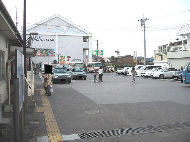 タクシーや自転車の親子が行き交う豊四季駅北口のロータリーと、正面に建つ大型のスポーツクラブの建物