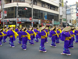 紫と黄色の浴衣に編み笠をかぶった踊り手が路上で列をつくって踊る様子