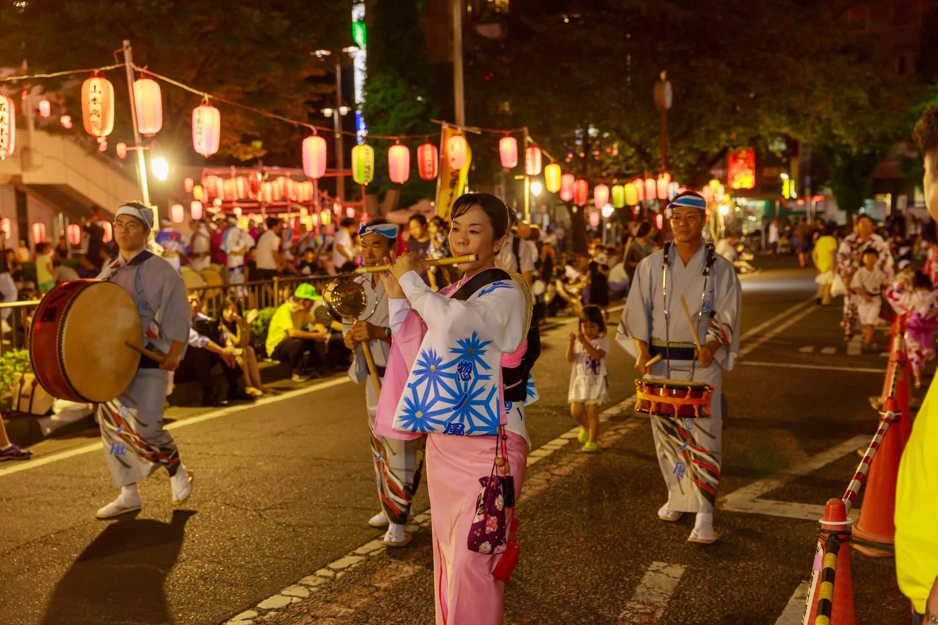 阿波踊りのお囃子隊。笛を吹く女性を中心に、鉦や太鼓の奏者が続き、頭上にはカラフルな提灯が連なる