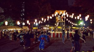 夜のやぐらを囲んで浴衣姿の人々が輪になって踊る盆踊りの様子