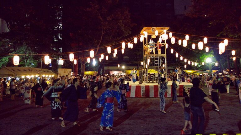 夜のやぐらを囲んで浴衣姿の人々が輪になって踊る盆踊りの様子