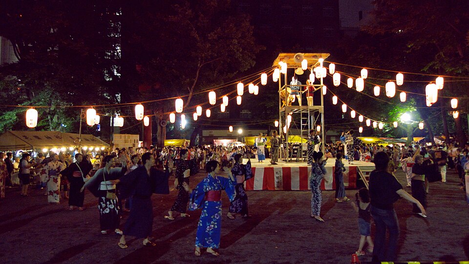夜のやぐらを囲んで浴衣姿の人々が輪になって踊る盆踊りの様子