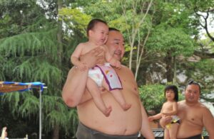 諏訪大神の境内で力士が泣く赤ちゃんを高く抱え上げる様子