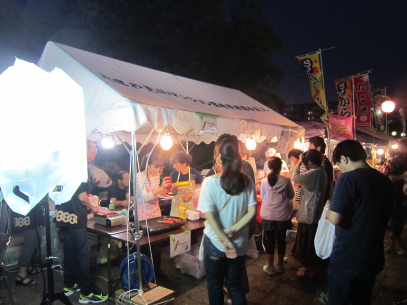 真砂夏祭りの屋台。白いテントで法被姿のスタッフが調理し、来場者が列をつくる