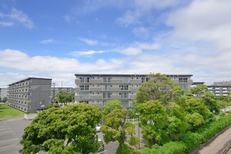 千葉幸町団地の住棟外観。5階建ての中層住棟が並び、手前に駐車場と大きな街路樹が写る