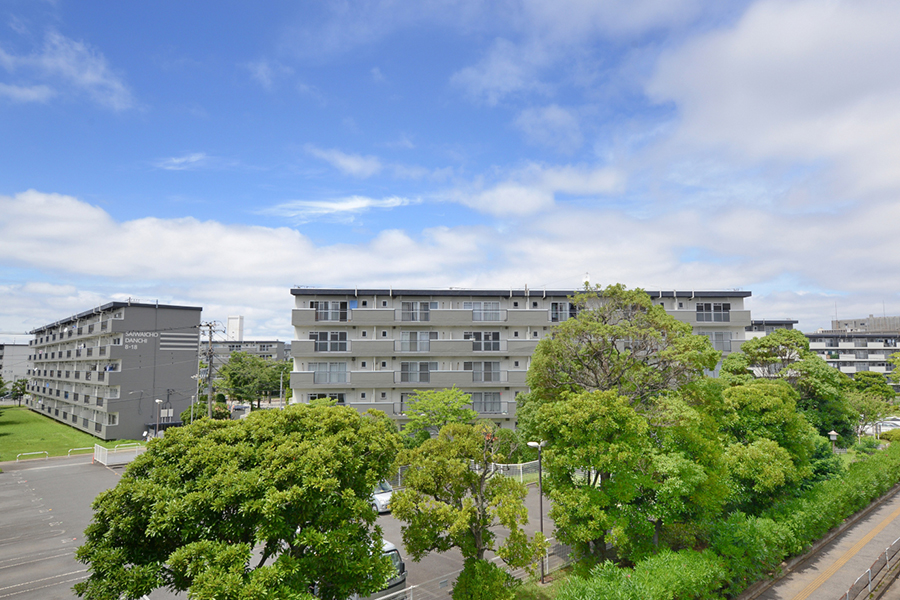 千葉幸町団地の住棟外観。5階建ての中層住棟が並び、手前に駐車場と大きな街路樹が写る