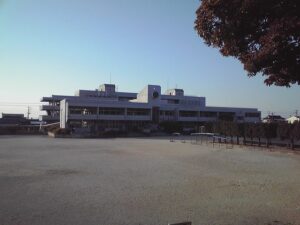 広い土のグラウンドの奥に白い3階建ての校舎が建ち、右手に鉄棒とうんていが並ぶ袖ケ浦市立昭和小学校の校庭