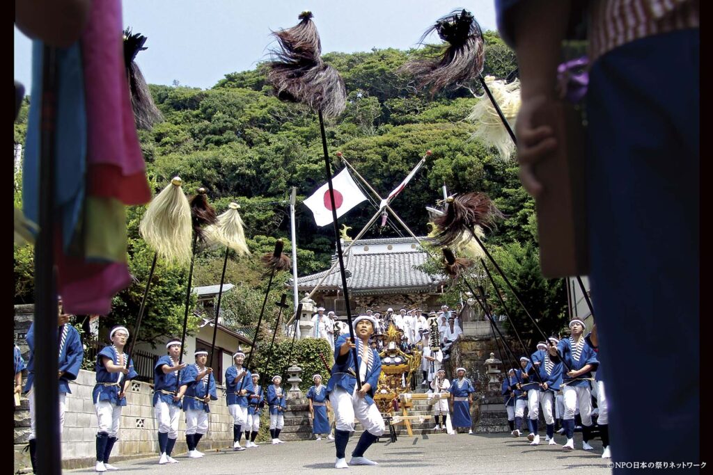 鵜原の大名行列で毛槍や沙熊を掲げて進む青い法被姿の男衆と、後方の神輿・社殿