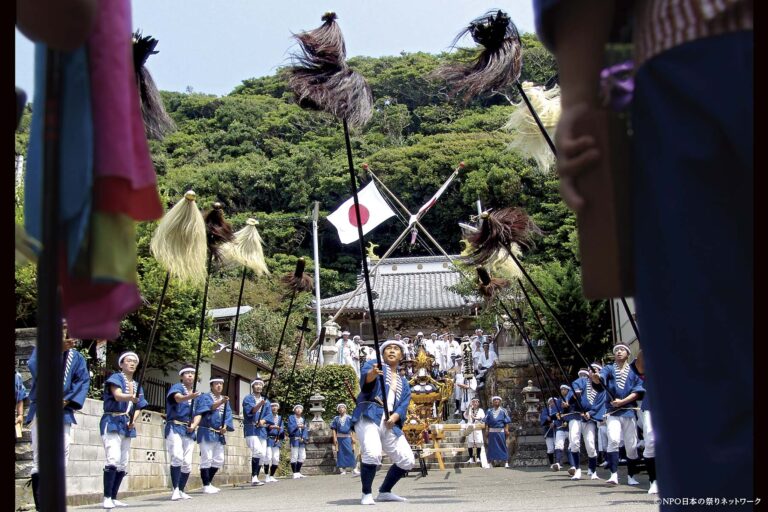 鵜原の大名行列で毛槍や沙熊を掲げて進む青い法被姿の男衆と、後方の神輿・社殿