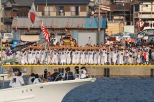 勝浦漁港の岸壁に白い法被姿で並ぶ担ぎ手と、接岸した漁船