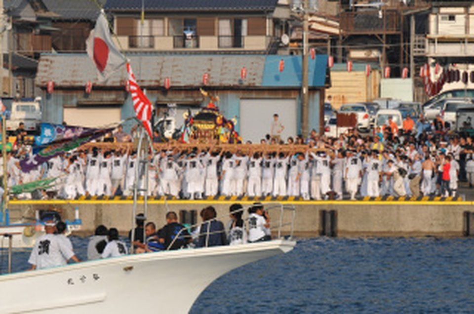 勝浦漁港の岸壁に白い法被姿で並ぶ担ぎ手と、接岸した漁船