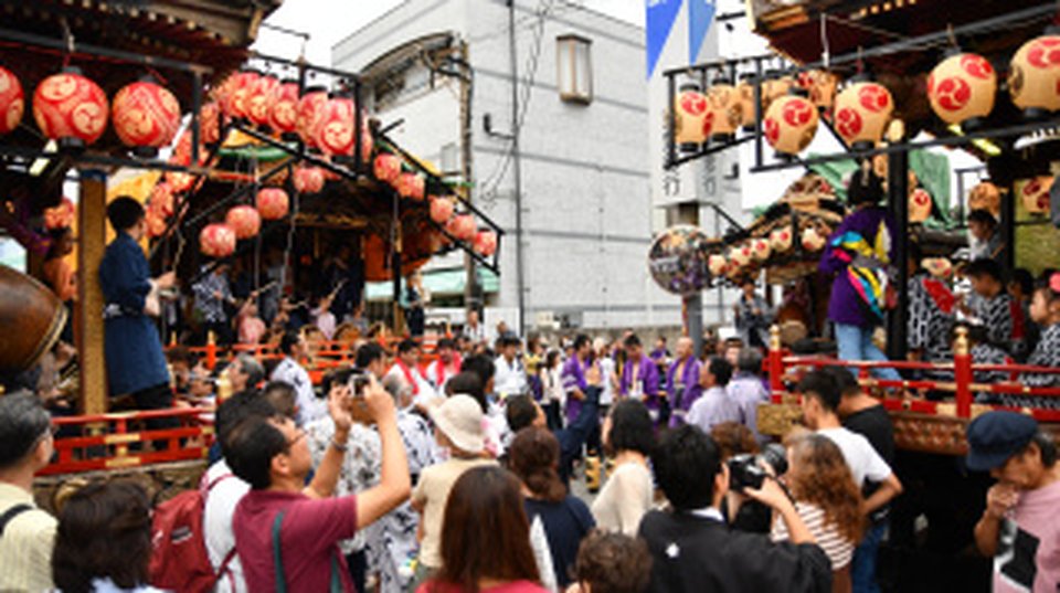 赤い提灯を吊るした屋台が2台向かい合い、大勢の観客が囲む夜の商店街