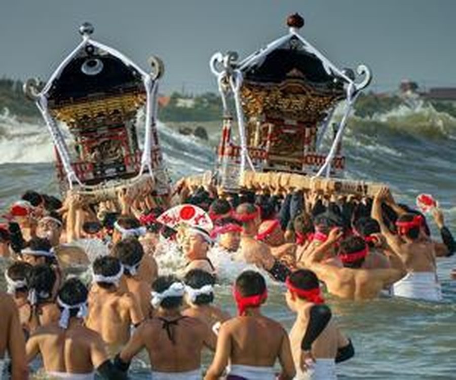 波の立つ海の中に、黒漆に金の装飾をつけた神輿2基が並んで担がれている。白い鉢巻きや赤い鉢巻きを締めた担ぎ手が腰まで海に浸かって密集し、両手を上げている。奥は白波と水平線