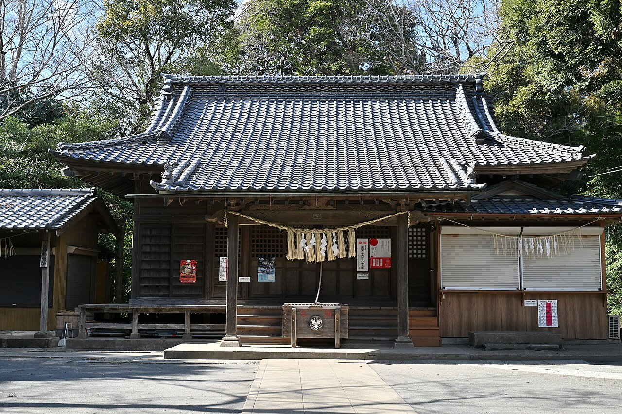 竹内神社の拝殿。瓦葺きの入母屋屋根が重なる木造の社殿で、正面の軒下にしめ縄と白い紙垂が下がり、中央に賽銭箱が置かれている。右手には白いシャッターの授与所が並ぶ
