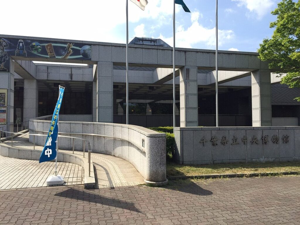 千葉県立中央博物館の正面入口。石張りの外壁に館名が刻まれ、青いのぼり旗と掲揚ポールが並ぶ