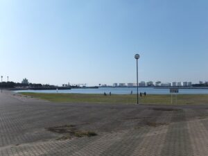 千葉ポートパークの海沿い。手前にレンガ調の広い舗装、奥に芝生と街灯、水面の向こうに白い球形タンクや港湾設備