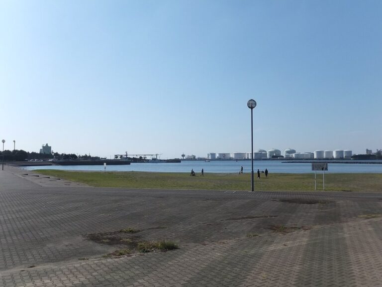 千葉ポートパークの海沿い。手前にレンガ調の広い舗装、奥に芝生と街灯、水面の向こうに白い球形タンクや港湾設備
