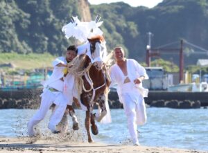 岩瀬海岸の砂浜を走る神馬。白い御幣を背に立てた馬の手綱を、白装束の若衆2人が両脇から取って並走している