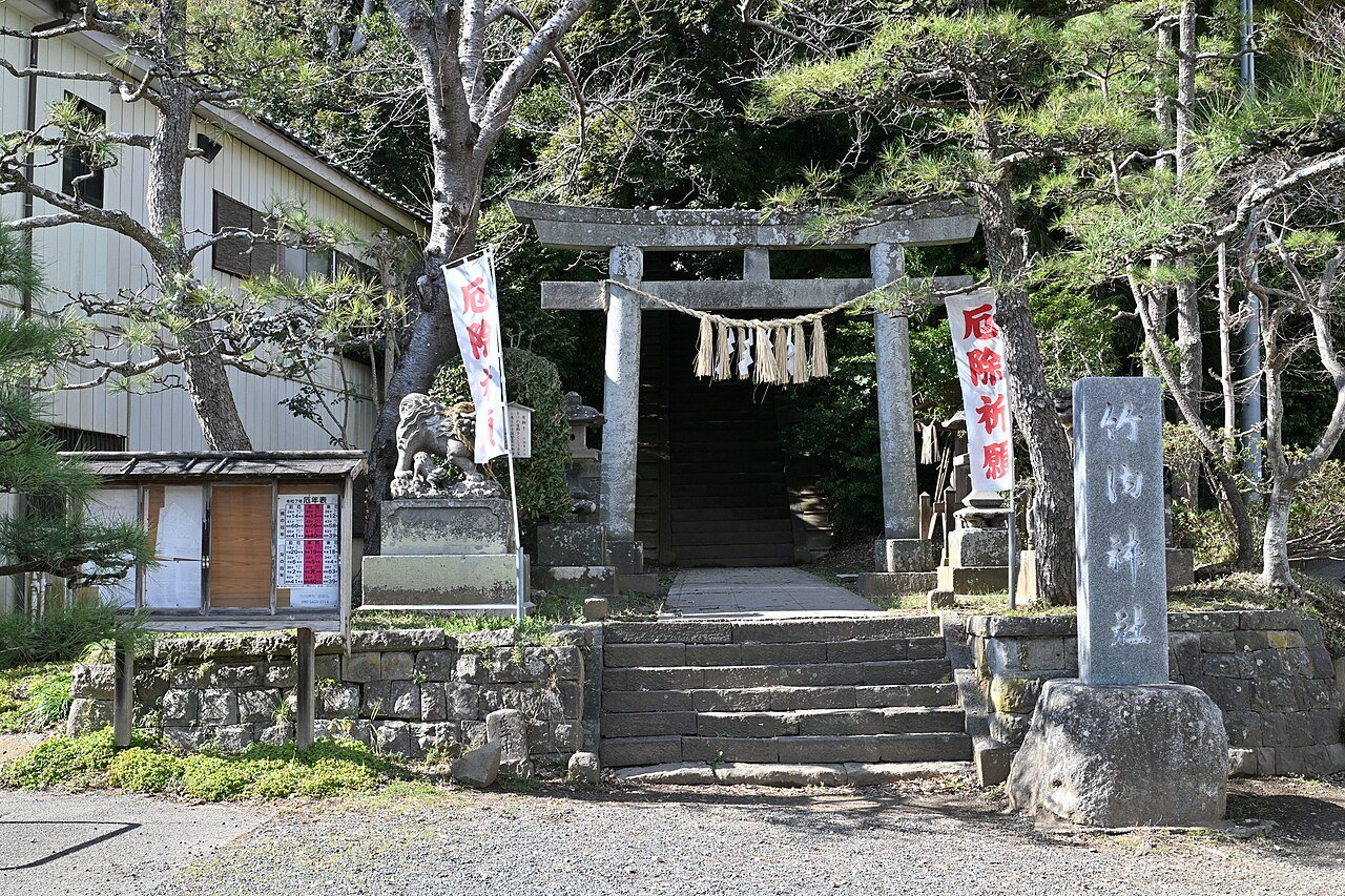 竹内神社の石鳥居。しめ縄が張られた鳥居の奥に石段が上へ続き、左に狛犬、右に「竹内神社」と刻まれた社号標が立つ。鳥居の両脇には「厄除祈願」と朱書きされた白いのぼりが2本はためいている