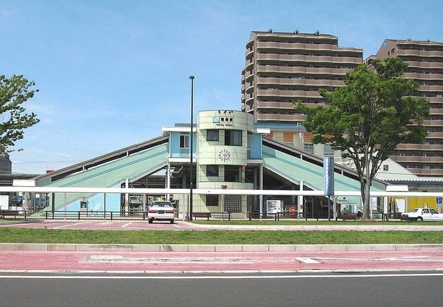 君津駅南口の駅舎。三角形の大きな屋根とスロープ状の通路をもつ建物で、背後に高層マンションが並ぶ