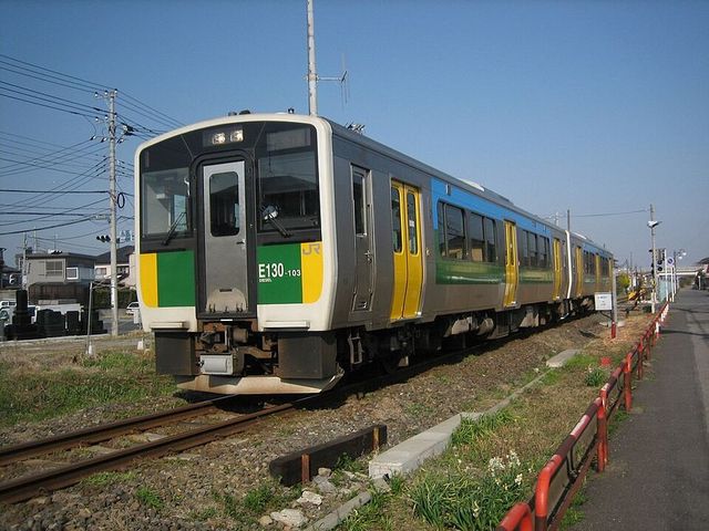 久留里線を走るキハE130系気動車。黄色と緑の帯を巻いた2両編成が単線の線路を走っている