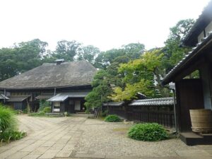 旧吉田家住宅の敷地。左奥に茅葺きの大屋根をのせた主屋、右手に瓦屋根の建物と塀が並び、手前は石畳と砂利敷きの前庭