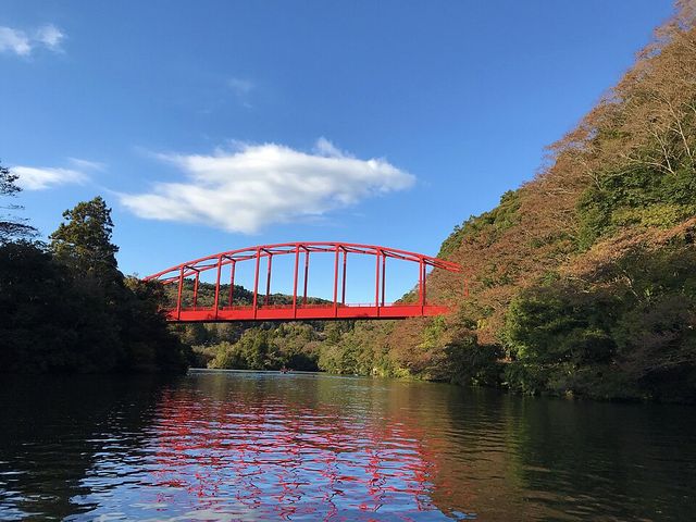 亀山湖の水面と、湖にかかる赤いアーチ橋。両岸は色づき始めた山に囲まれている