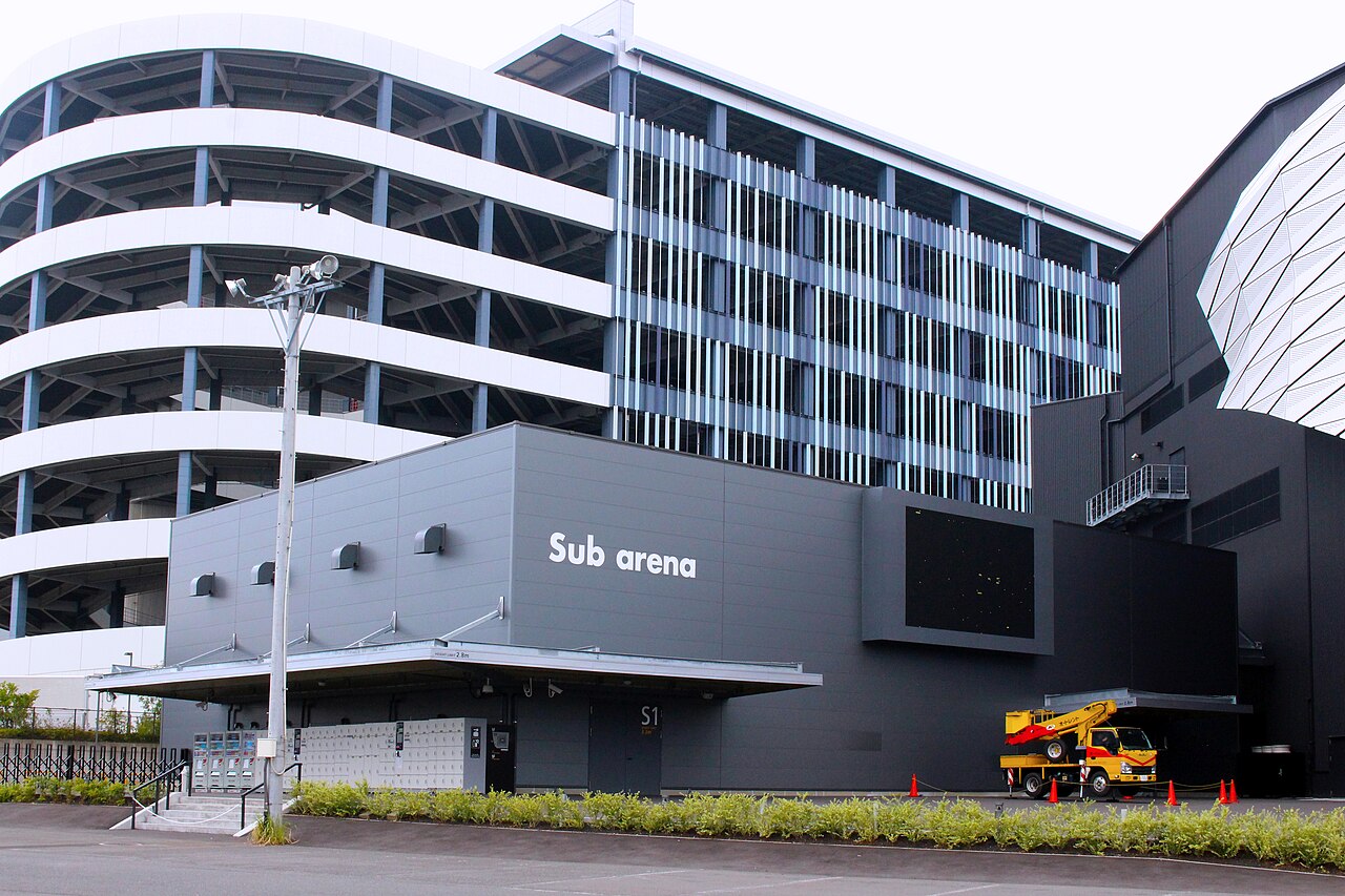 サブアリーナの外観。灰色の壁に「Sub arena」の白い表示があり、その左手前の庇の下に白いコインロッカーが並ぶ。奥にららぽーとの立体駐車場が重なって見える