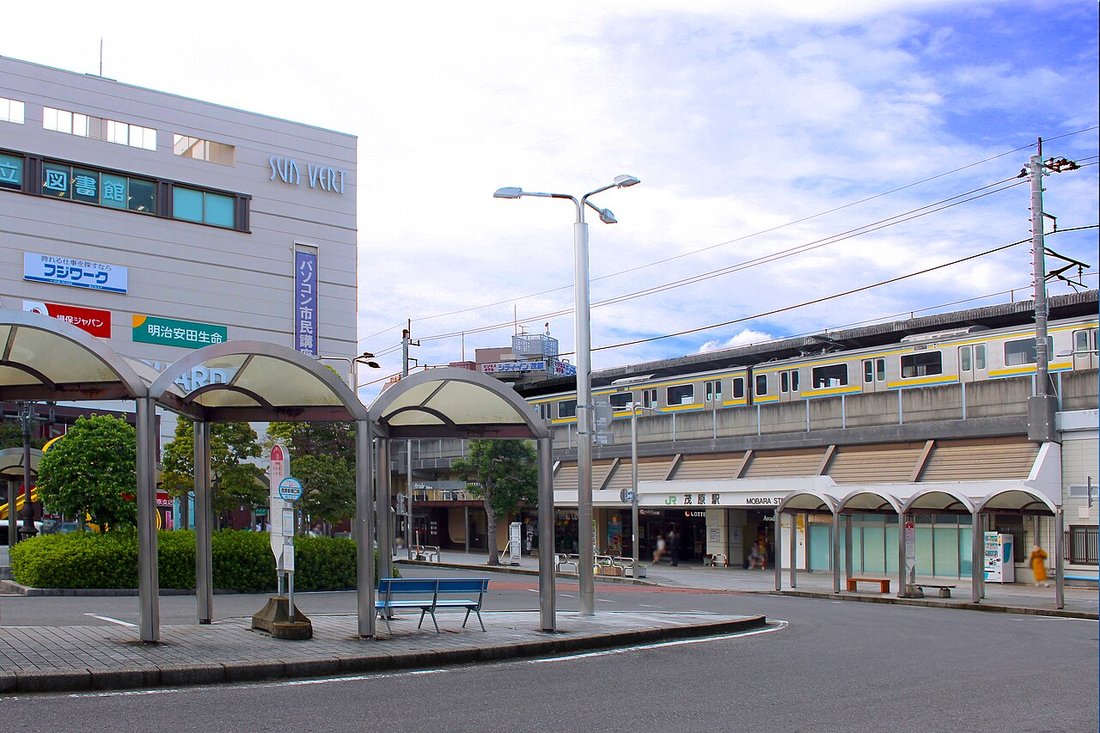 JR茂原駅南口の駅前広場。アーチ屋根のバス待合所が並び、右奥に高架の駅舎と停車中の黄色い帯の電車