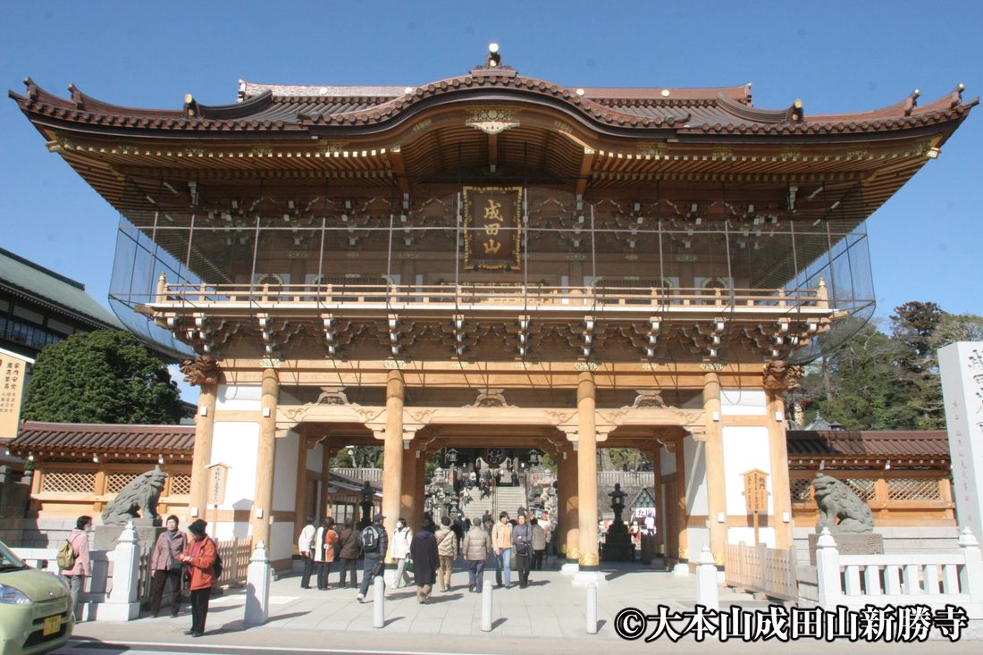 成田山新勝寺の総門。木造の大きな門の下を参拝者が通り、門の奥に石段と次の門が見える